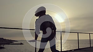 Girl with a sports figure and short hair incendiary dancing booty dance on the pier near the sea at sunset