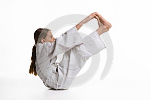 A girl in a sports kekogi reaches her hands at her feet, waving a stretch