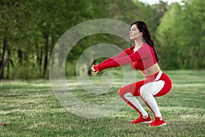 Girl in a sports suit does squats, physical exercises on a background of nature. The concept of a healthy lifestyle, exercise,