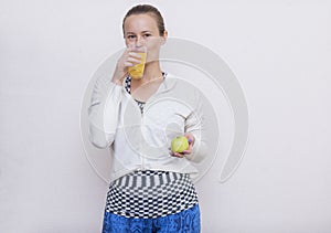 Girl in a sports top drinking orange juice, holding an Apple
