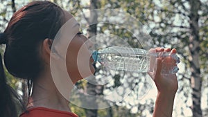 A girl after sports, unscrews the lid and drinks water on the street.