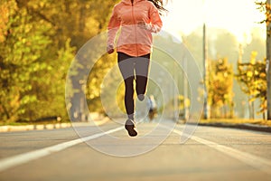 A girl in sportswear runs on the road in the autumn park.