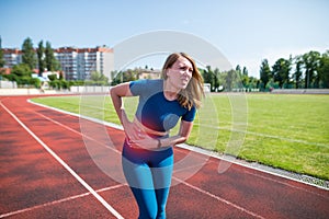 Girl in sportswear in stadium is exhausted and has pain during training and workout