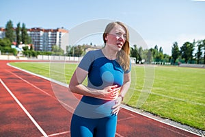 Girl in sportswear in stadium is exhausted and has pain during training and workout