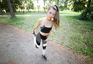 Girl in sportswear stretches leg muscles in park.