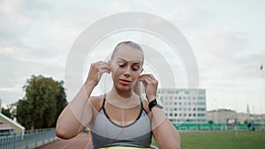 Girl sportswoman puts on pink headphones. The girl is preparing to run. Slow motion.