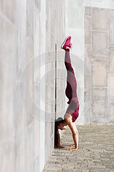 A girl with a sporty build performs a handstand exercise on a street playground