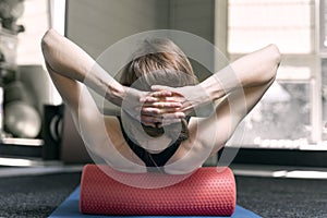 Girl with sporty physique makes myofascial release of the back with foam roller. Roller for physiotherapy