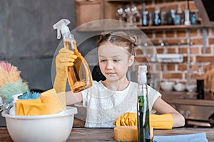 Girl with spray bottles and different cleaning supplies at home