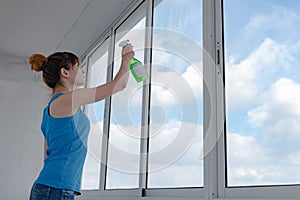 The girl sprays liquid for washing windows on dirty glass.