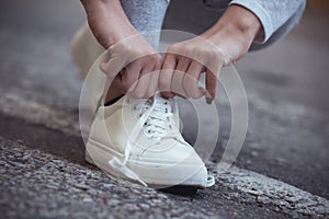 Girl squatted down to tie shoelaces on white sneakers on asphalt road, autumn sport concept outdoors