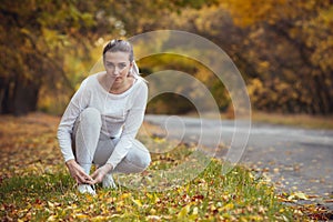 Girl squatted down to tie shoelaces on white sneakers on asphalt road, autumn sport concept outdoors