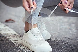 Girl squatted down to tie shoelaces on white sneakers on asphalt road, autumn sport concept outdoors