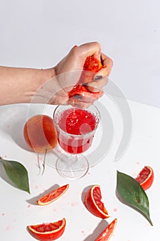 The girl squeezes the juice from the orange hand in a glass. Cut oranges on a light background