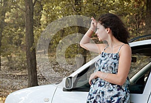 Girl stand on country road near auto look into the distance, big high trees, summer season