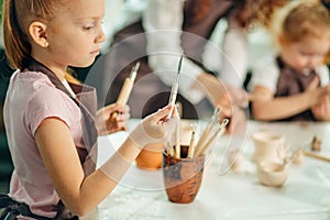 Girl stand near table and choose knife to work with clay