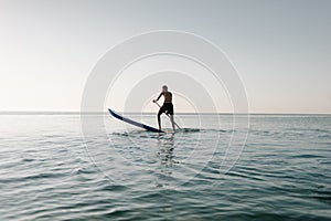 Girl stand up paddle boarding sup on quiet sea at sunset