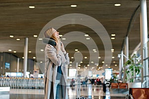 Girl standing in airport hall with valise and neck pillow.