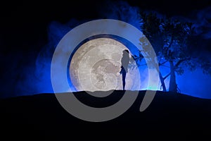 Girl standing alone behind big full moon. Dark toned foggy background. Loneliness bad mood concept