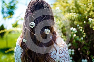 Girl standing back to camera with white spirea flowers in dark long wavy hair. Spring blossoming and tenderness