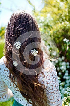 Girl standing back to camera with white spirea flowers in dark long wavy hair. Spring blossoming and tenderness