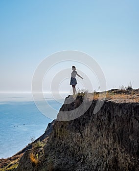 The girl is standing on a cliff near the sea