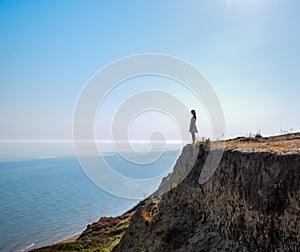 The girl is standing on a cliff near the sea