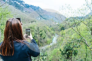 A Girl Standing on the Cliff and Taking Photograph of the Valley with the River. Red head making picture with smart phone to Tara