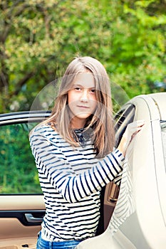 Girl standing close to the car looking at camera. Summertime out