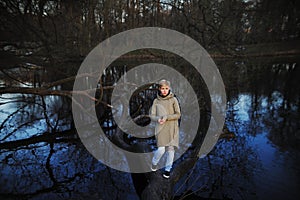 Girl standing on a fallen tree near the pond in early spring