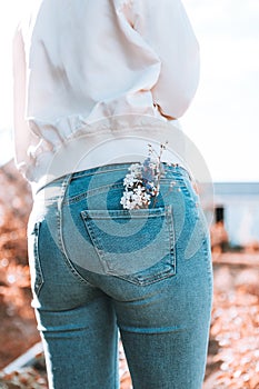 The girl is standing with her back in blue jeans, flowers in her pocket