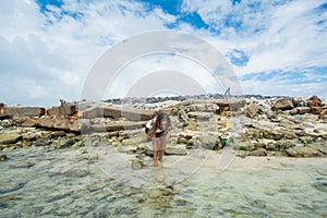 Girl standing looking for shells in the ocean with garbage dump at background