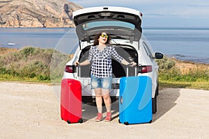 Young woman standing near back of car smiling and getting ready to go. Summer road trip photo