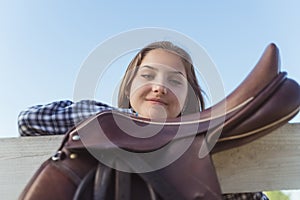 Girl Standing Near A Leather Saddle Hanging On The Wooden Fence In The Ranch