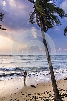 Girl standing near seashore with palm at sunrise