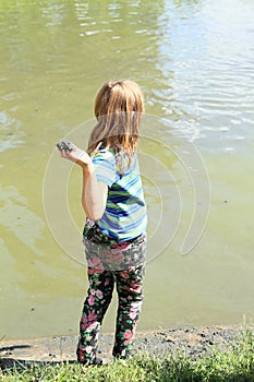 Girl standing by pond and throwing mud