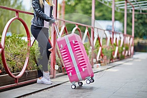 A girl is standing by the railing with a pink suitcase