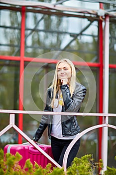 A girl is standing by the railing with a pink suitcase