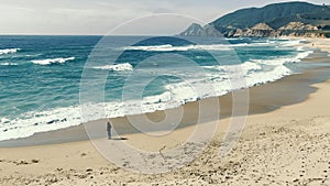 A girl standing on the shore of a sandy beach of the Pacific Ocean. Big waves come to the shore. Sunny day.