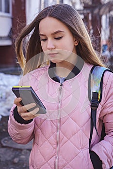 The girl is standing on the street and holding the phone