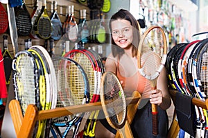 Girl standing in t-shirt in sporting goods store with racket