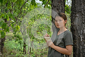The girl is standing, taking notes in a small note book in the green forest photo