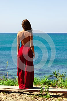 Girl standing topless in red skirt above the sea looking