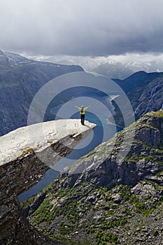 Girl standing on Trolltunga rock (Troll\'s Tongue rock) and makes the photo with the Norwegian mountain landscape
