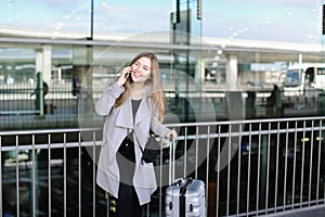 Girl standing with valise and talking by smartpone near airport.