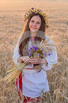 Girl standingwith sheaf on wheat field at sunset