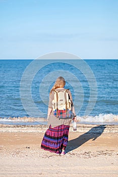 A girl stands back and looks at the sea. Hippie Girl looks at the sea. Woman with a bottle of wine is by the sea. hippie