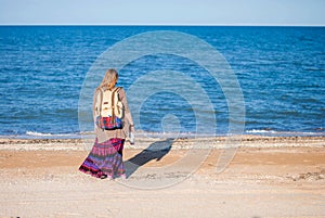 A girl stands back and looks at the sea. Hippie Girl looks at the sea. Woman with a bottle of wine is by the sea. hippie
