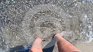 Girl stands bare feet on sandy beach and buries its fingers in sand