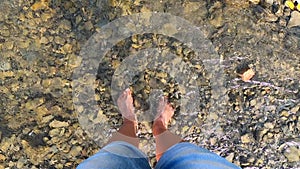 Girl stands barefoot on stones shallow river